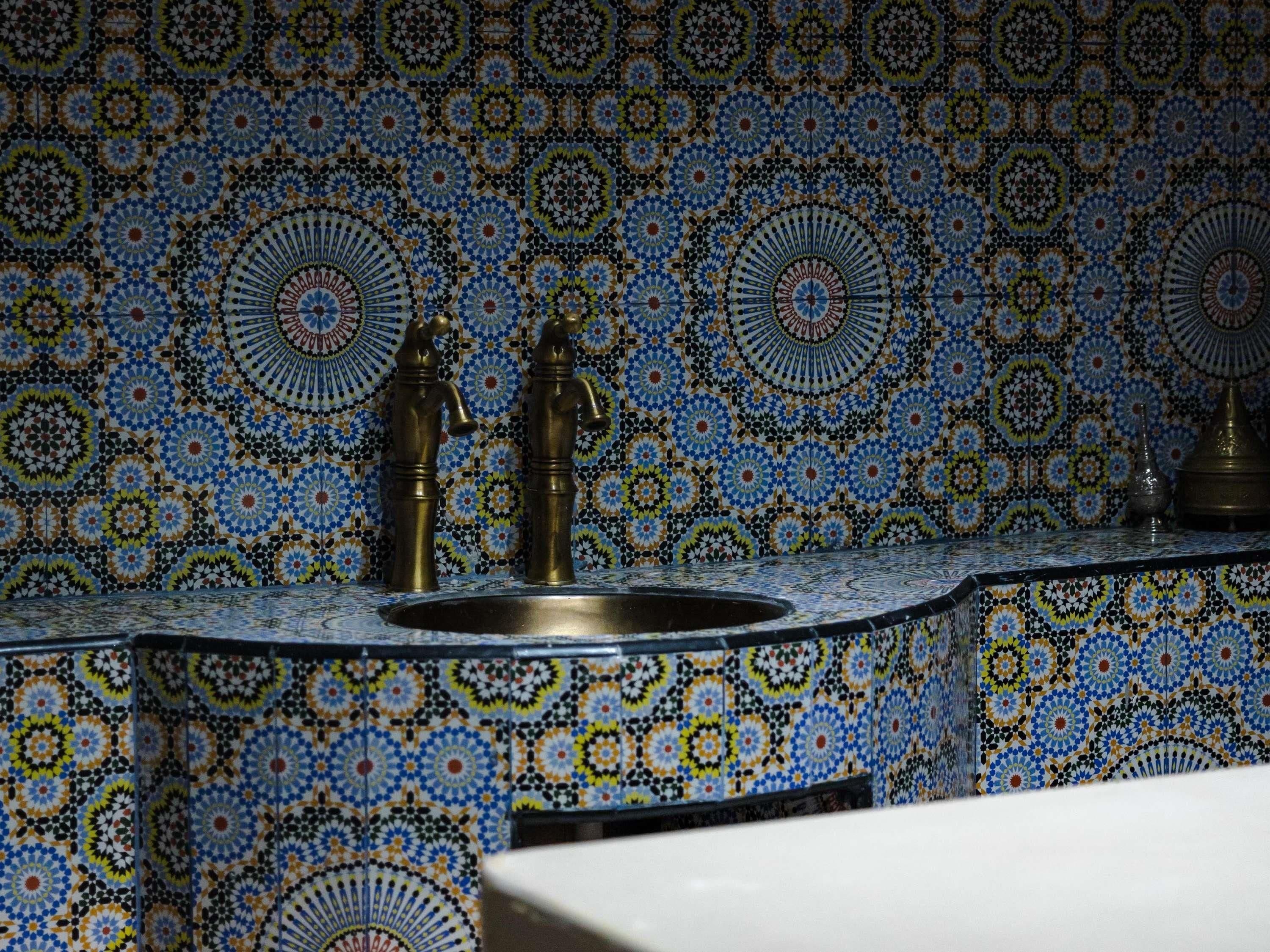 A bathroom with a sink and two faucets, surrounded by intricate tile patterns.