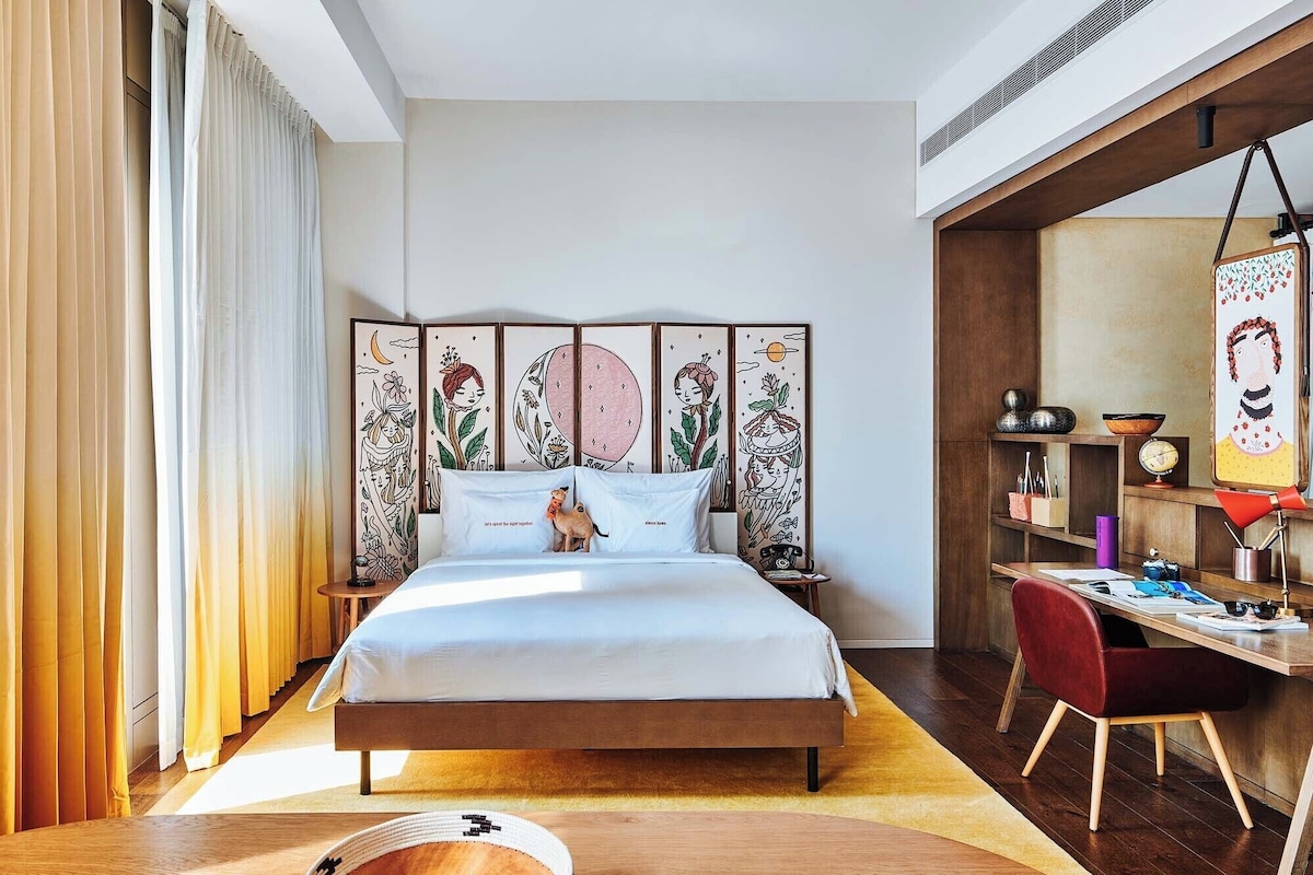 A modern bedroom with a large bed, a desk, and a bookshelf.