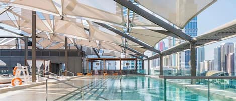 Una piscina infinita en la azotea con vistas a un horizonte urbano, sillones de descanso y una zona cerrada con vidrio.