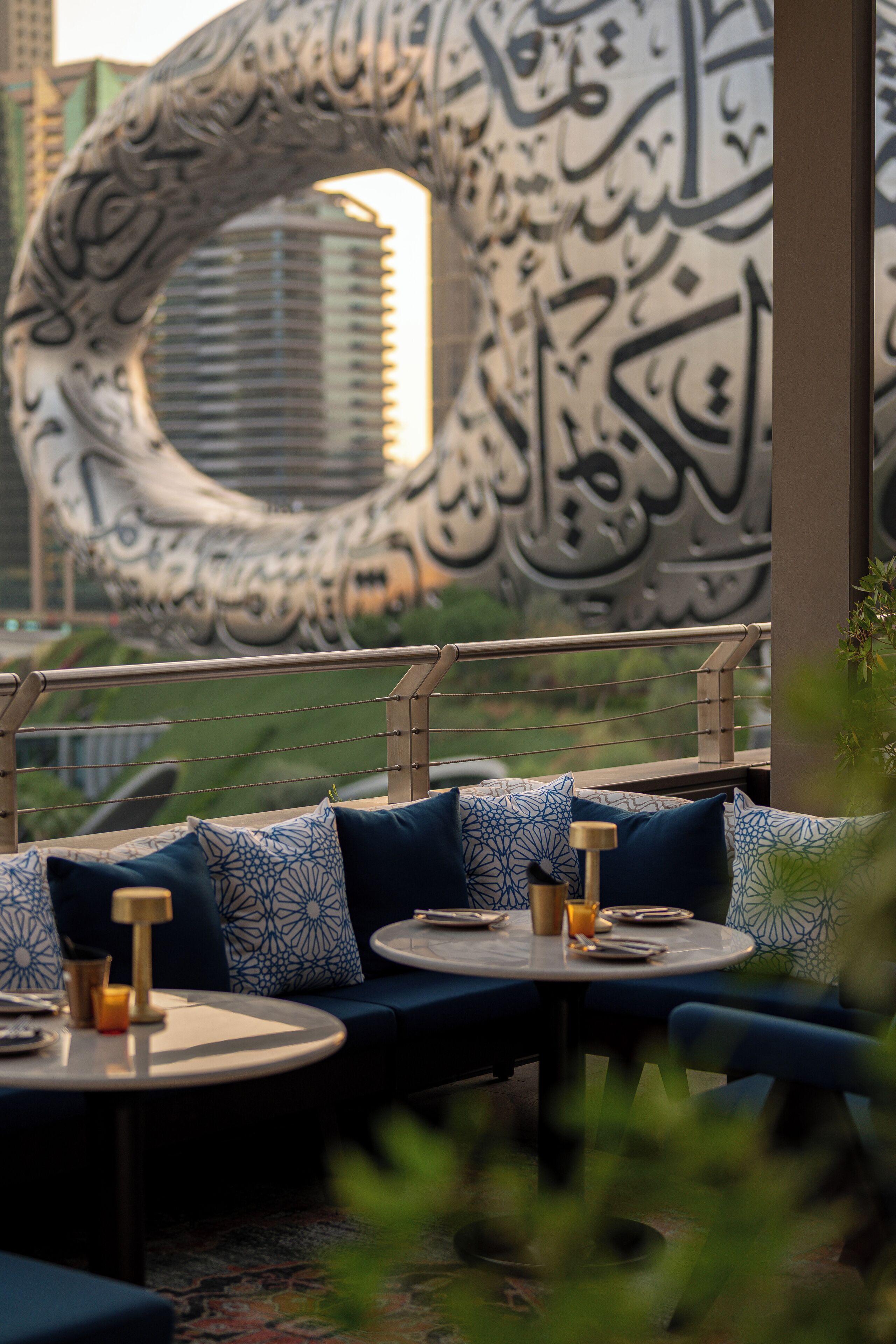 A modern outdoor seating area with patterned cushions and round tables, featuring a large decorative wall with calligraphy.