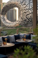 A modern outdoor seating area with patterned cushions and round tables, featuring a large decorative wall with calligraphy.
