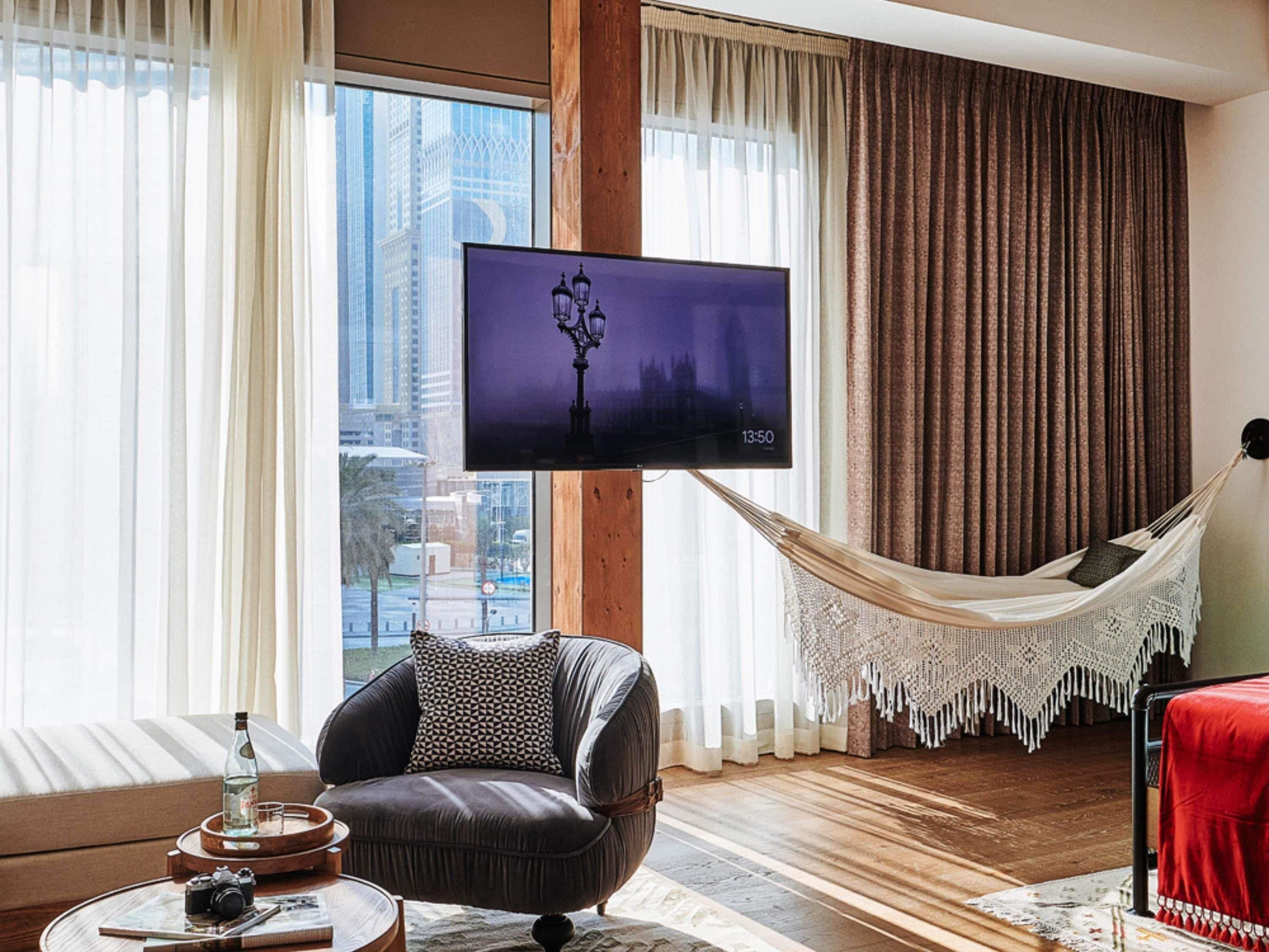A living room with a large window, a flat-screen TV, a comfortable chair, a hammock, and a red table.