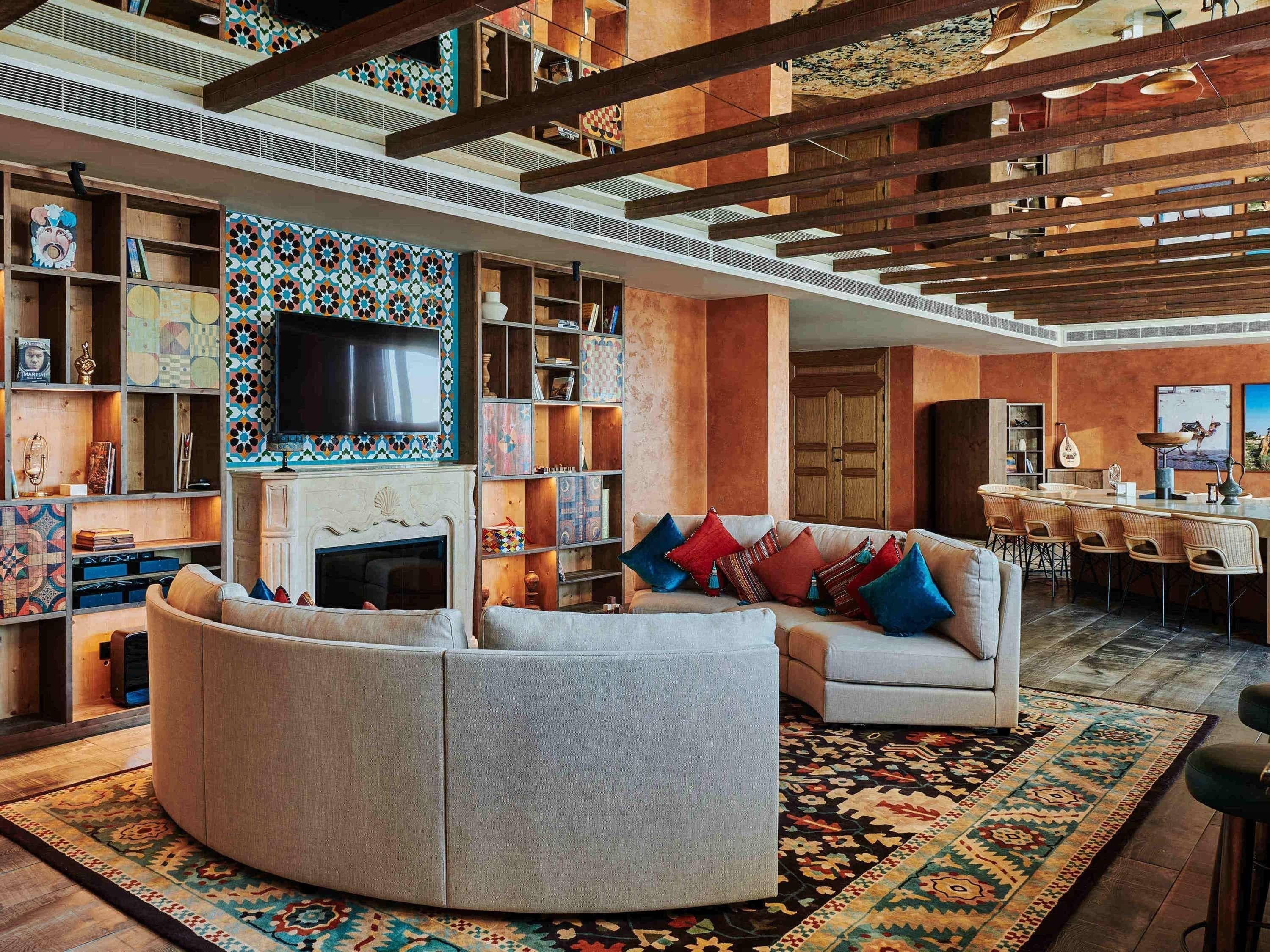 A modern living room with a sectional sofa, a fireplace, and a large TV. There are bookshelves and a coffee table with decorative items.