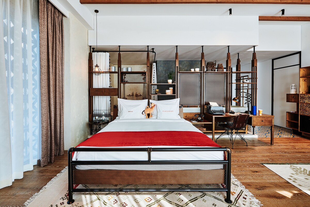 A modern bedroom with a large bed, a desk, and a shelving unit.
