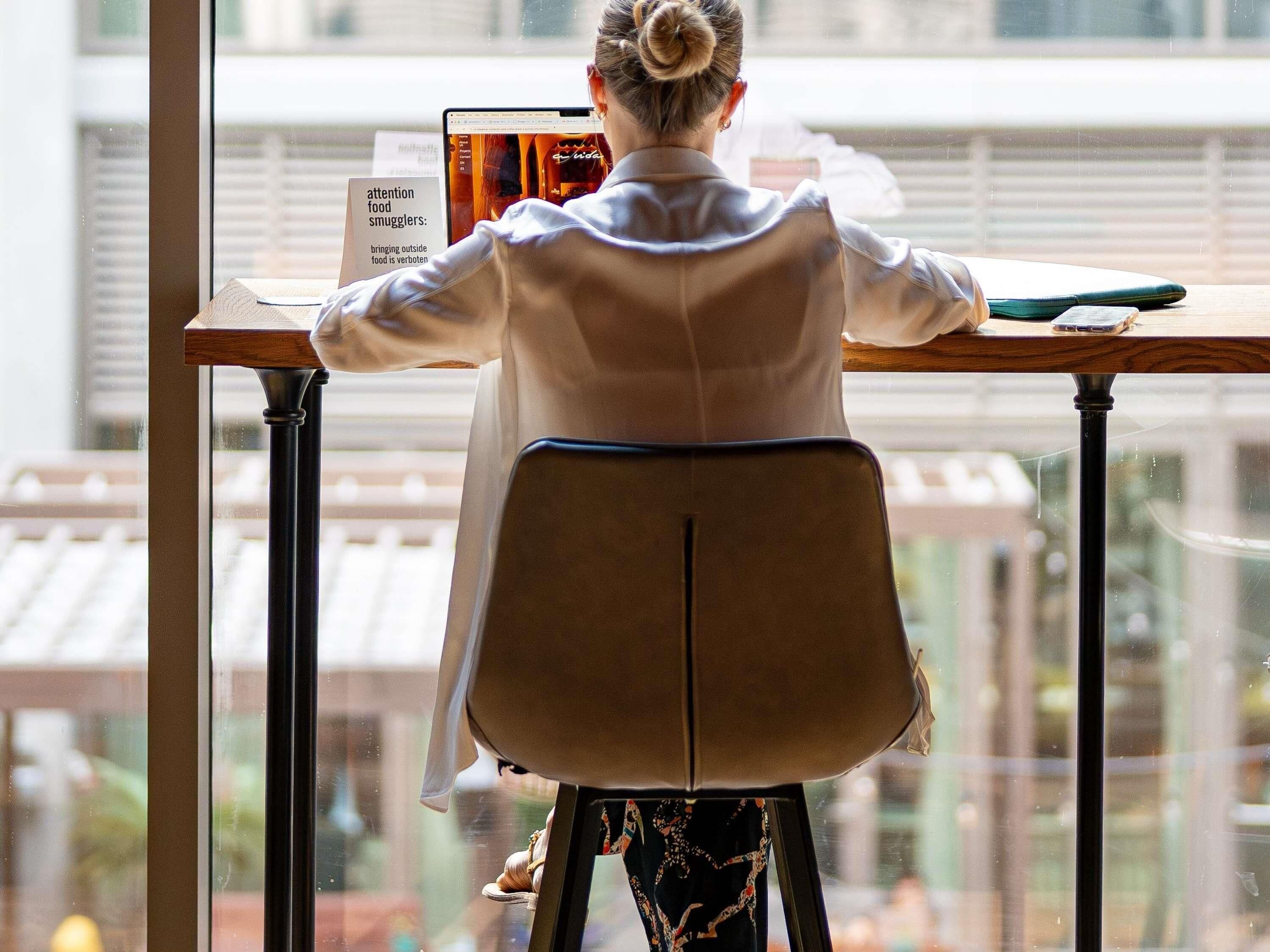 A person seated at a table with a laptop, a sign about food smuggling, and a window with a view of buildings.