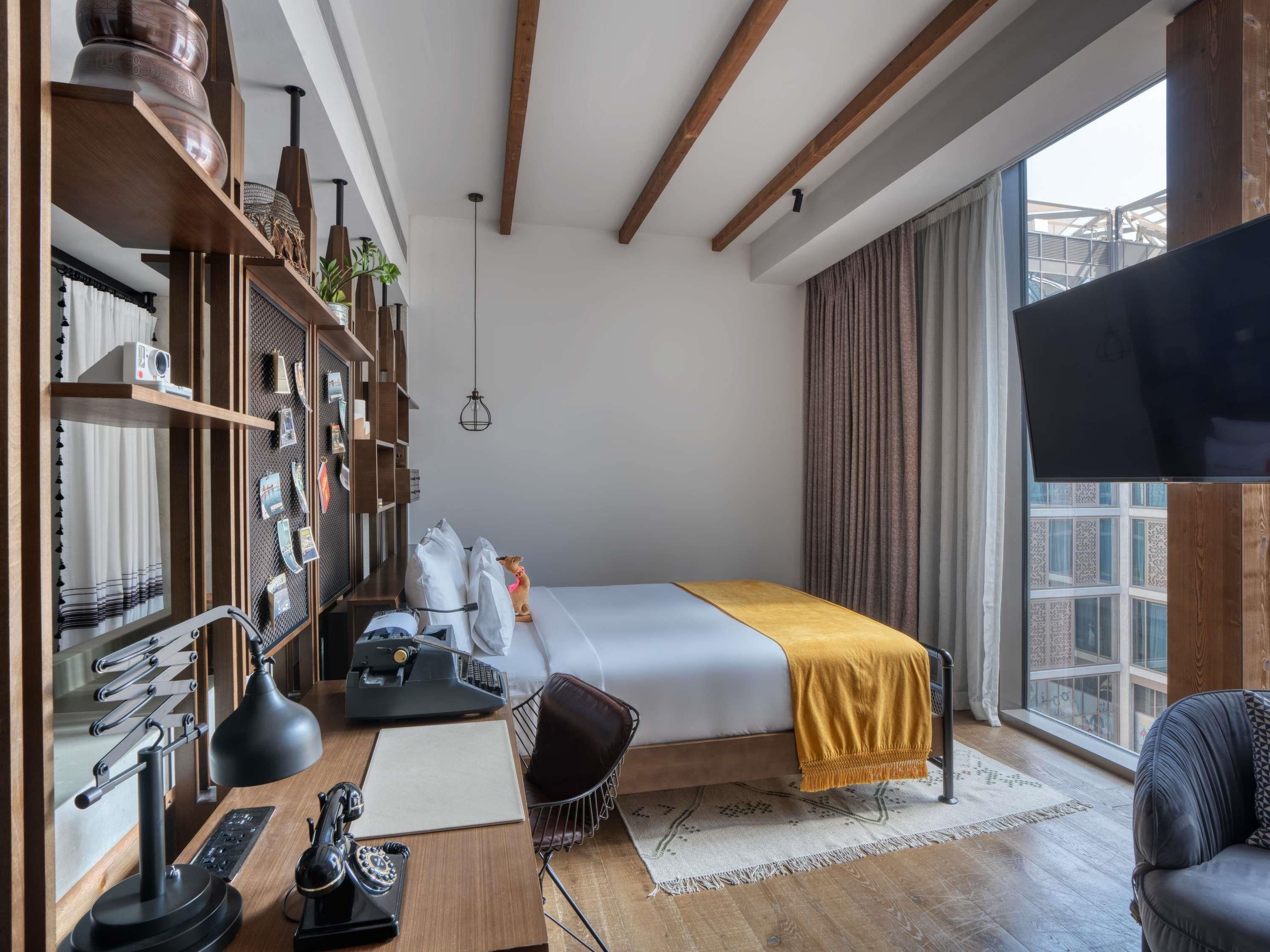 A modern hotel room with a bed, desk, chair, and large window.