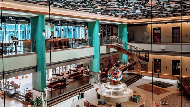 Un amplio atrium con techo alto que presenta un mural con temática espacial, varios niveles con zonas de estar y una distribución circular central para sentarse.