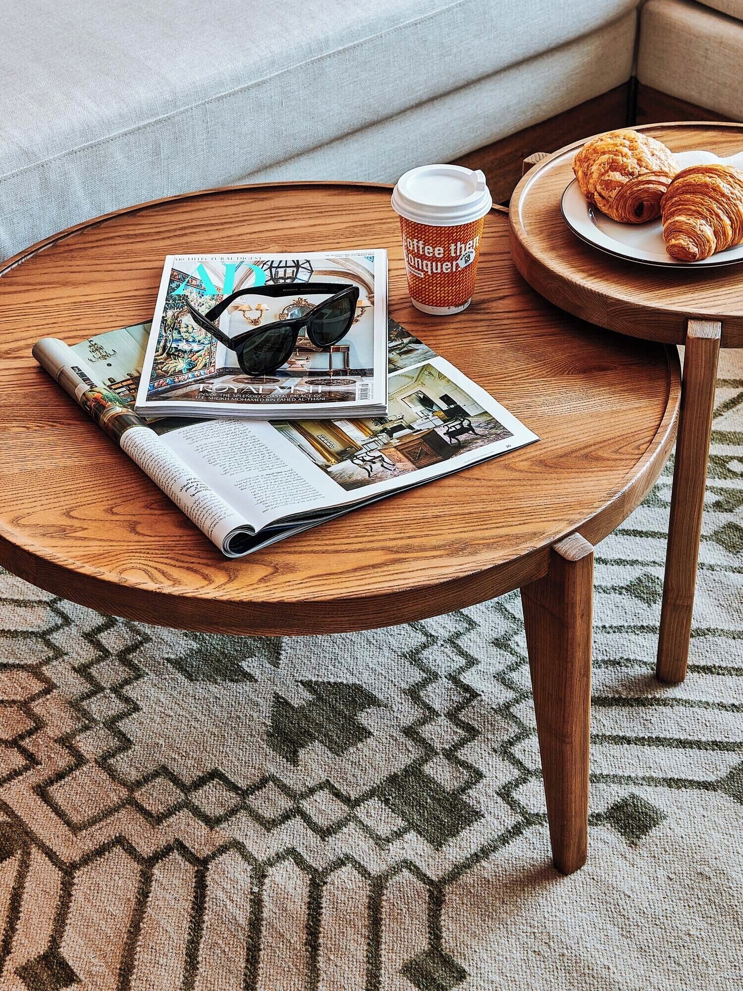 Mesa de madeira redonda com uma revista, óculos de sol e uma xícara de café.