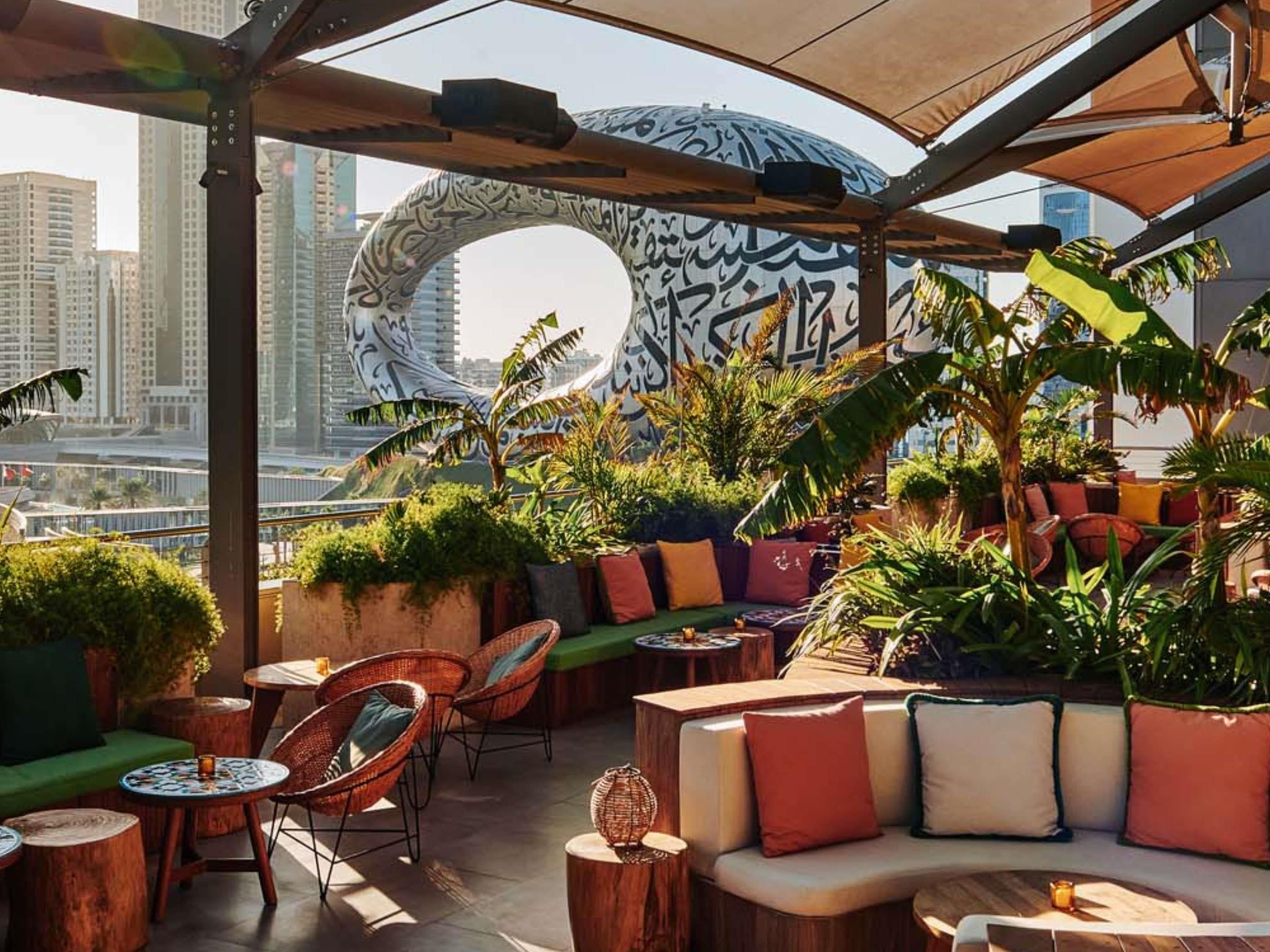 An outdoor seating area with wicker chairs, a cushioned bench, and potted plants.