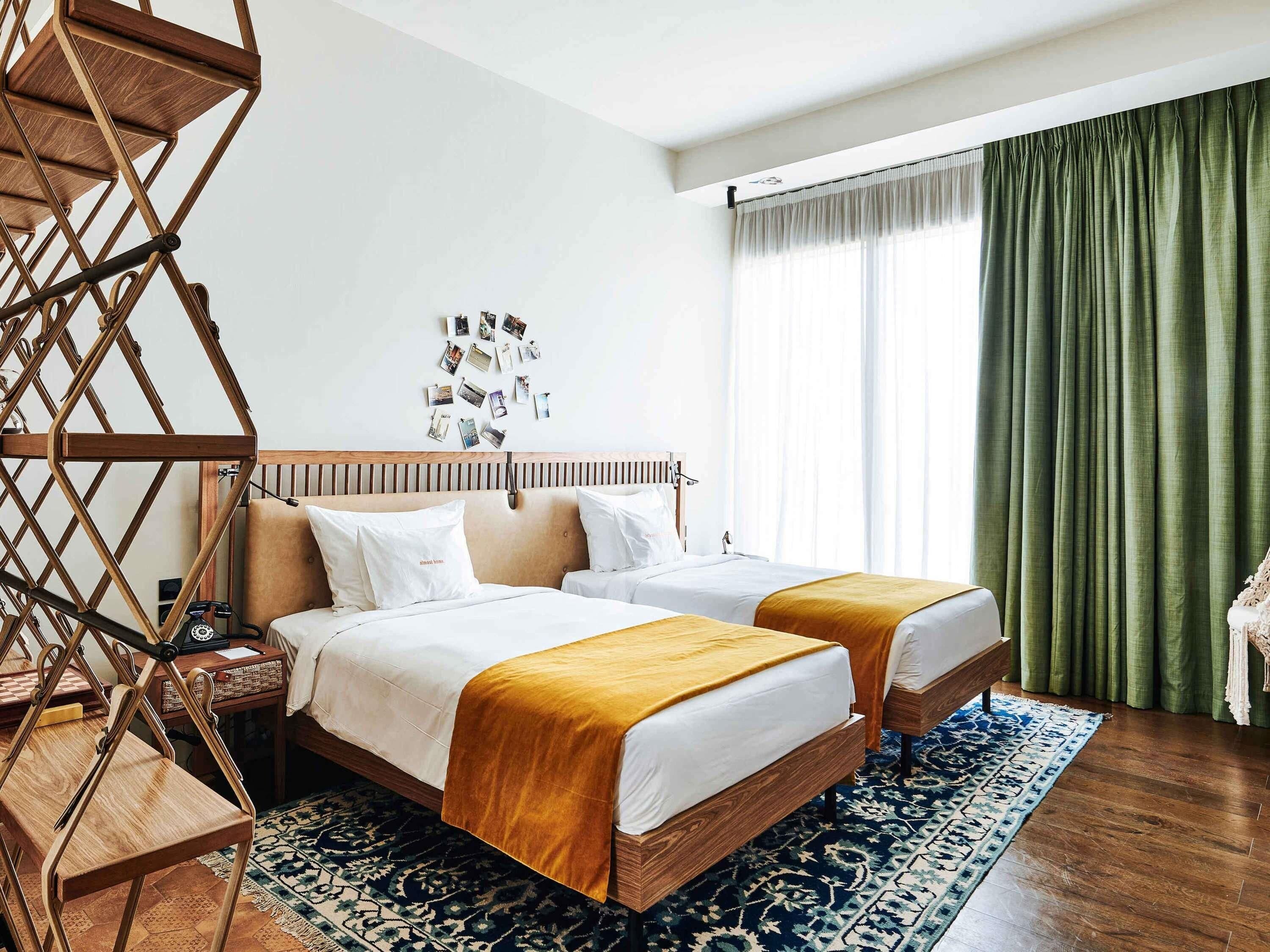 Ein Hotelzimmer mit zwei Betten, einem hölzernen Kopfteil, einem gemusterten Teppich und einem grünen Vorhang.
