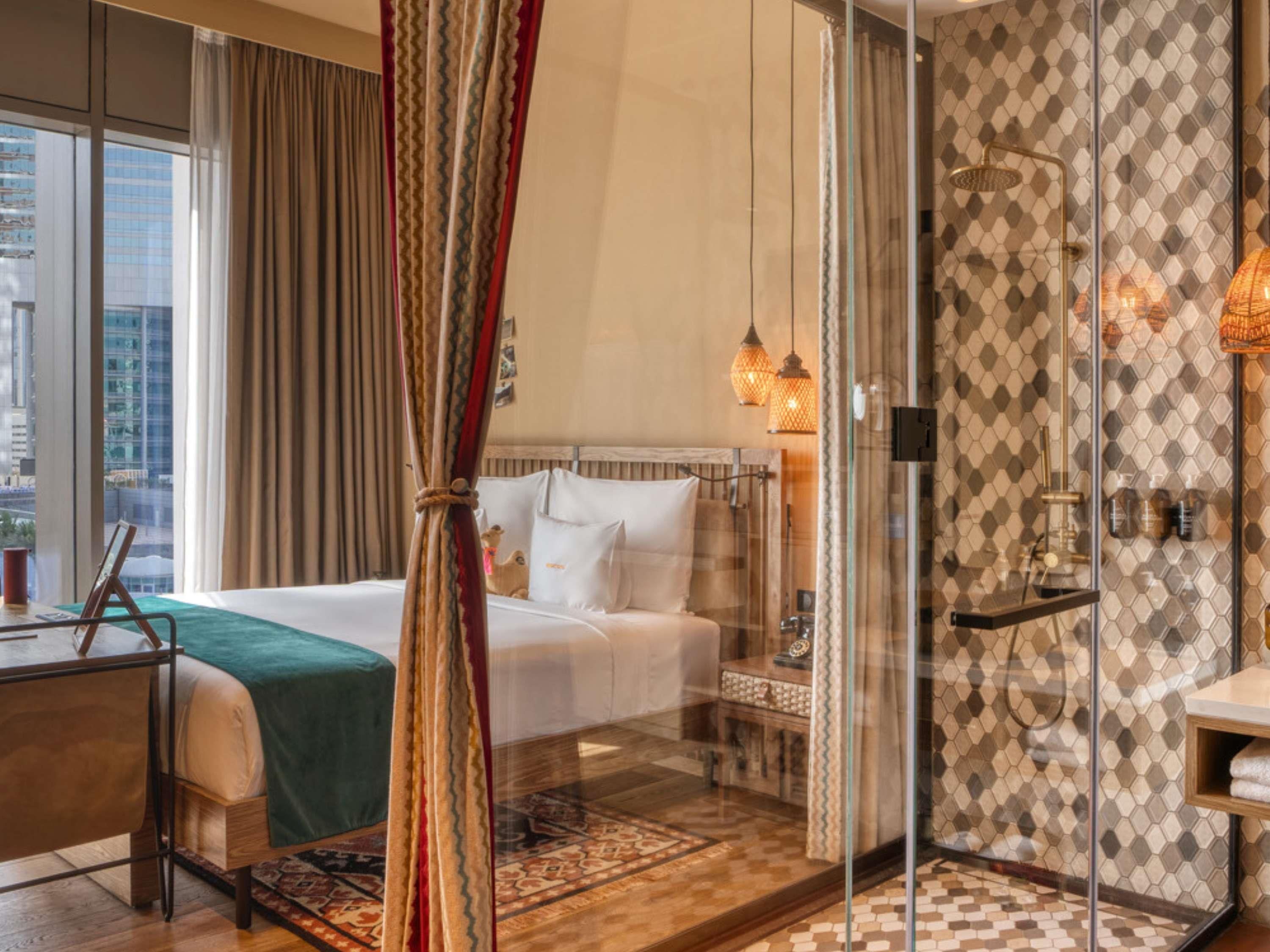 Ein Hotelzimmer mit Bett, Schreibtisch, Duschkabine und Blick auf die Stadt.