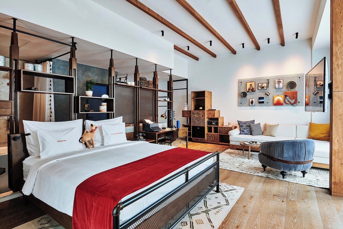 A modern bedroom with a large bed, built-in shelving, a desk, and a seating area with a sofa and armchair.