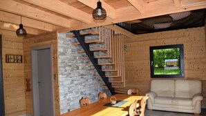 A wooden interior with a dining table, chairs, a sofa, a staircase, and a window with a view. - Vosges mountain chalet (Ban-sur-Meurthe-Clefcy)