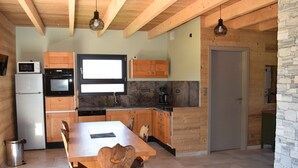 A modern kitchen with wooden cabinets, a built-in oven, and a dining area with a table and chairs. - Vosges mountain chalet (Ban-sur-Meurthe-Clefcy)