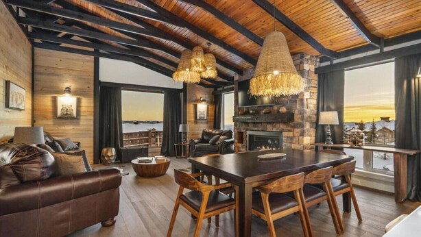 A spacious living area with a large wooden dining table, leather sofa, and a fireplace.