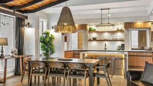 A modern kitchen with a central island, wooden chairs, and a hanging light fixture.