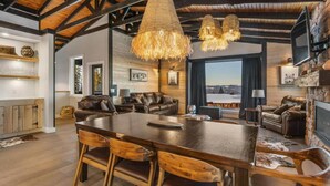 A spacious living area with a large wooden dining table, leather sofas, and a fireplace.