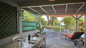 Ein überdachter Patio-Bereich mit Esstisch für zwei Personen, einer Hängematte und einem Liegestuhl.