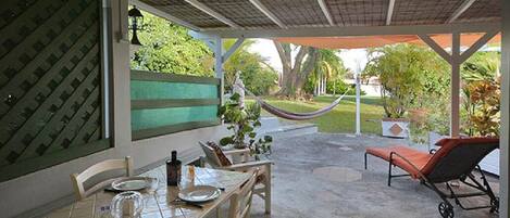 A covered patio area with a dining table set for two, a hammock, and a lounge chair.