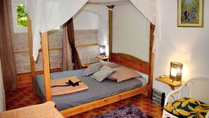 Ein Bett mit Baldachin, ein Nachttisch mit Lampe und ein Sessel mit gemustertem Kissen.