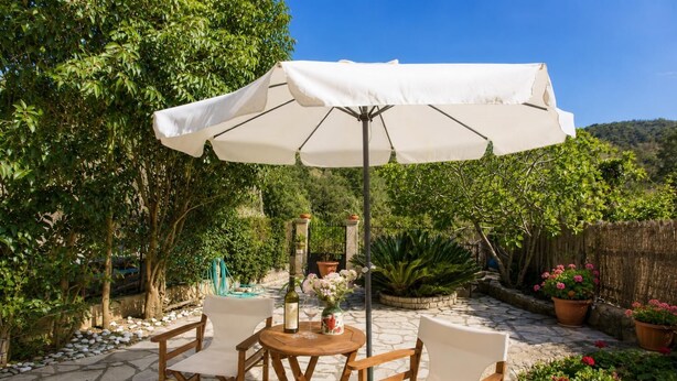 Une terrasse extérieure avec une table et des chaises, un parasol blanc et des plantes en pot.