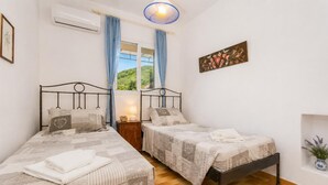 Une chambre avec deux lits, une fenêtre avec des rideaux, un climatiseur fixé au mur et une petite table de chevet avec une lampe.