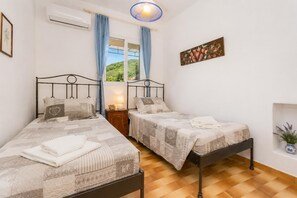 Une chambre avec deux lits, une fenêtre avec des rideaux, un climatiseur fixé au mur et une petite table de chevet avec une lampe.
