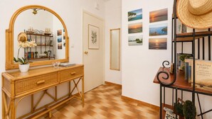 Un couloir doté d'un plancher en bois, d'un miroir, d'une console en osier ornée d'une plante en pot et d'un mur décoré de tableaux encadrés.