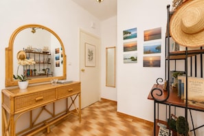 Un couloir doté d'un plancher en bois, d'un miroir, d'une console en osier ornée d'une plante en pot et d'un mur décoré de tableaux encadrés.