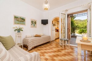 A cozy room with a bed, a chair, a small table with a candle, and a TV. - Effie Apartment - One Bedroom Apartment, Sleeps 2 (Corfu)