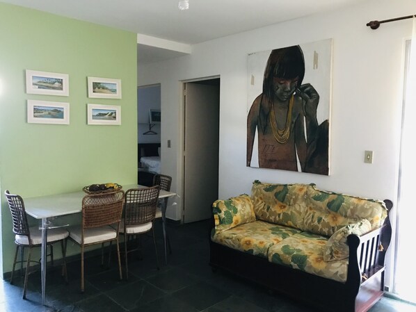 A living area with a sofa, dining table, chairs, and artwork on the walls. - PET Family (Ubatuba)