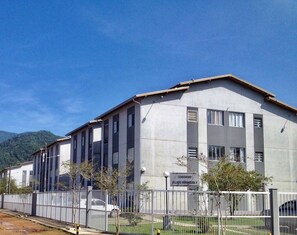 A large building with a flat roof and multiple windows, surrounded by a fence and trees. - PET Family (Ubatuba)