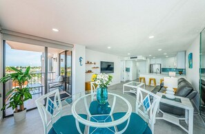 Un espai de vida modern amb un balcó, zona de dinar, cuina i zona d'estar amb sofà.