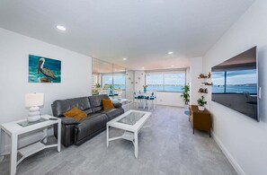 A modern living room with a leather sofa, a glass coffee table, and a dining area with a view of the sea.