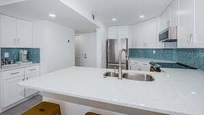 A modern kitchen with white cabinetry, a stainless steel refrigerator, and a speckled backsplash. - Waterfront 1BR condo with balcony, pool, hot tub, and resort perks in St. Petersburg. (St Petersburg)