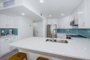 Una cucina moderna con mobili bianchi, un frigorifero in acciaio inox e una schiena di cucina decorata.
