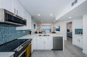 A modern kitchen with white cabinetry, a black range hood, and a backsplash with a blue mosaic pattern.