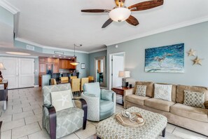 A spacious living room with a ceiling fan, a dining area with wicker chairs, and a kitchen in the background. - P4-1106 Blue Bliss at Portofino with Gulf View! (Pensacola Beach)