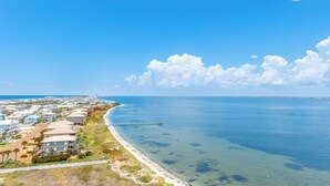 Une zone côtière avec une plage, un ciel bleu dégagé et une jetée qui s’avance dans l’eau.