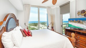 Habitación de hotel con una cama grande, ventilador de techo, televisión y vista a la playa y al océano.