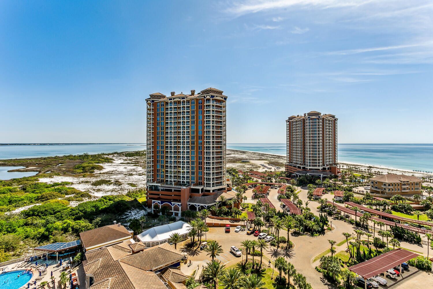 A resort with two tall buildings, a beach, and a pool area.