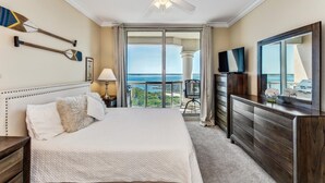 A hotel room with a large bed, a ceiling fan, a TV, a dresser, and a view of the ocean. - Last Minute Rates! Tower 4 2B Island View at Portofino! (Pensacola Beach)