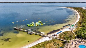 A coastal area with a dock, inflatable rafts, a sandy beach, and a pool. - Last Minute Rates! Tower 4 2B Island View at Portofino! (Pensacola Beach)