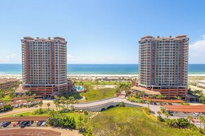 A high-rise hotel with a beach view, multiple balconies, and a parking area.