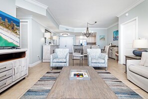 A living room with a TV, two armchairs, a coffee table, and a dining area in the background.