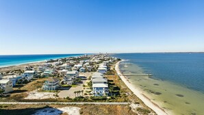 A coastal residential area with houses along the beachfront, a pier extending into the water, and a clear blue sky.