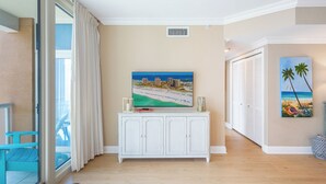 A hotel room with a large window, a white cabinet with a painting, and a door leading to a balcony. - Great Gulf Views @ Portofino 4-1606! (Pensacola Beach)