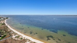 Een kustgezicht met een helder strand, een steiger die het water in reikt, en een verre kustlijn.