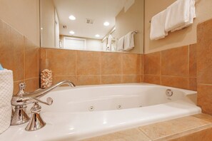 A modern bathroom with a large bathtub, a mirror, and beige tiled walls.