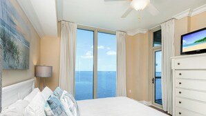 Een slaapkamer met een groot bed, een plafondventilator, een televisie en uitzicht op zee.